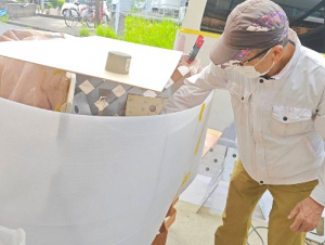 塗料が周辺に飛び散らないよう周りを囲い、その中でスプレーしている様子